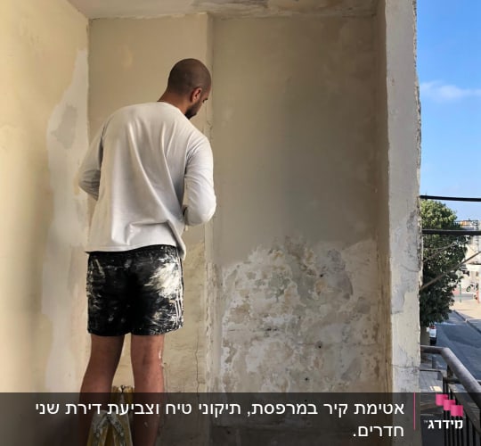 אדם עומד על סולם ומכין קיר לצביעה